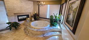 Primary bathroom featuring an inviting chandelier, a bathtub, and a multi sided fireplace