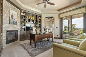 Office space featuring light colored carpet, a raised ceiling, a ceiling fan, and arched walkways