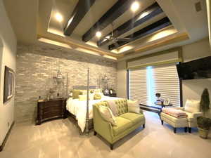 Carpeted primary bedroom with a raised beam ceiling, brick wall, and ceiling fan