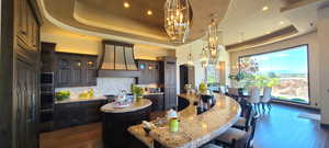 Kitchen featuring light stone countertops, premium range hood, a tray ceiling, a center island, and dark wood-type flooring