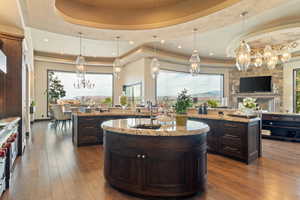Kitchen featuring a sink, dark wood-style flooring, a chandelier, a raised ceiling, and an island with sink