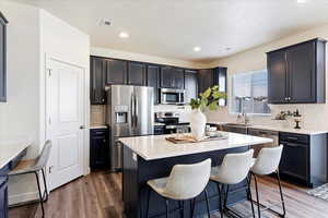 Kitchen featuring appliances with stainless steel finishes, farmhouse sink, laminate flooring, a kitchen breakfast bar, and productivity desk.