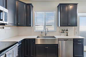 Kitchen featuring appliances with stainless steel finishes, farmhouse sink, laminate flooring, a kitchen breakfast bar, and productivity desk.