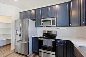 Kitchen featuring appliances with stainless steel finishes, farmhouse sink, laminate flooring, a kitchen breakfast bar, and productivity desk.