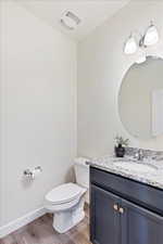 Half bathroom featuring vanity, toilet, and laminate flooring.