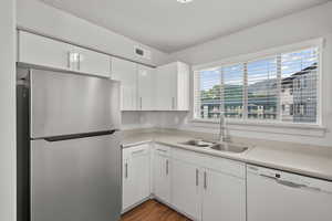 Kitchen with dark hardwood / wood-style floors, white dishwasher, stainless steel refrigerator, sink, and white cabinets