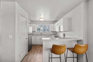 Kitchen with white appliances, a kitchen bar, wood-type flooring, kitchen peninsula, and sink