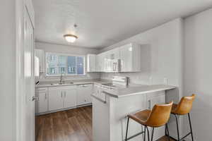 Kitchen featuring a kitchen bar, sink, white appliances, and white cabinetry