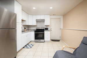 Kitchen featuring light tile patterned floors, white cabinetry, stainless steel appliances, and tasteful backsplash