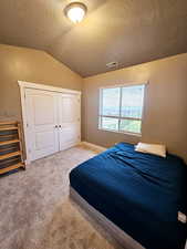 Carpeted bedroom featuring a textured ceiling, vaulted ceiling, and a closet