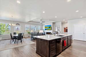 Kitchen with ceiling fan with notable chandelier, a center island with sink, sink, and light hardwood / wood-style floors