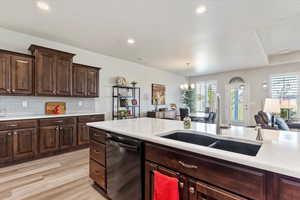 Kitchen featuring dishwasher, light hardwood / wood-style floors, a notable chandelier, sink, and dark brown cabinets