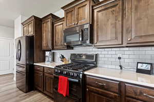 Kitchen with appliances with stainless steel finishes, light hardwood / wood-style flooring, backsplash, and dark brown cabinetry