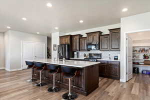 Kitchen featuring light wood-type flooring, backsplash, a kitchen breakfast bar, appliances with stainless steel finishes, and a center island with sink