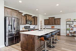 Kitchen featuring stainless steel appliances, light hardwood / wood-style floors, a kitchen island with sink, sink, and dark brown cabinetry