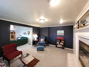 Living room with a textured ceiling, crown molding, a tile fireplace, and light colored carpet