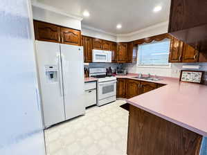 Kitchen with crown molding, white appliances, and sink