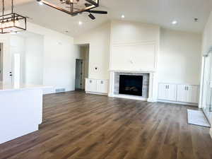 Unfurnished living room with ceiling fan with notable chandelier, high vaulted ceiling, and dark hardwood / wood-style flooring