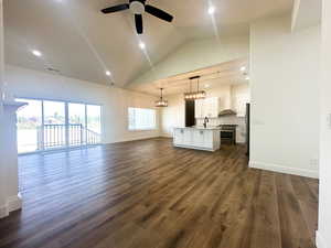 Unfurnished living room with dark wood-type flooring, ceiling fan, sink, and high vaulted ceiling