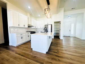 Kitchen with white cabinetry, dark hardwood / wood-style flooring, stainless steel appliances, and an island with sink