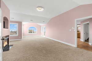 Unfurnished living room with light colored carpet and vaulted ceiling