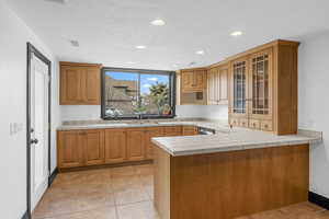 Kitchen with sink, kitchen peninsula, tile countertops, a textured ceiling, and light tile patterned flooring