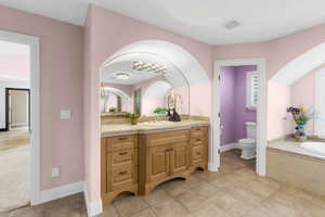 Bathroom featuring vanity, a relaxing tiled tub, and toilet