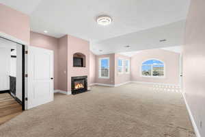 Unfurnished living room with a textured ceiling, light carpet, and lofted ceiling