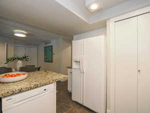 Kitchen featuring light stone counters, white appliances, and white cabinets