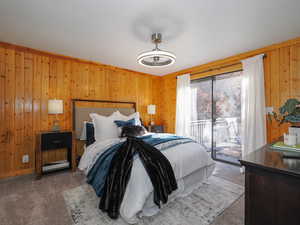 Carpeted bedroom featuring wood walls and access to exterior