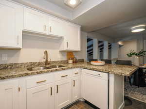 Kitchen with white dishwasher, kitchen peninsula, sink, white cabinetry, and light stone counters