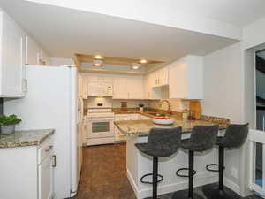 Kitchen with white appliances, white cabinetry, sink, kitchen peninsula, and a kitchen bar