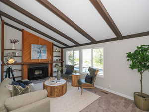 Living room with a fireplace, lofted ceiling with beams, and carpet floors