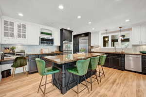 Kitchen with dark stone countertops, a center island, decorative light fixtures, stainless steel appliances, and a kitchen bar