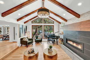 Living room with high vaulted ceiling, light hardwood / wood-style flooring, beam ceiling, and a tile fireplace