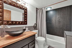 Full bathroom with toilet, shower / tub combo with curtain, a textured ceiling, and vanity