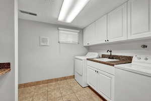 Laundry room with light tile patterned flooring, washer and dryer, cabinets, and sink