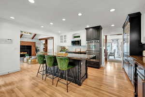 Kitchen with a large fireplace, a kitchen breakfast bar, a kitchen island, appliances with stainless steel finishes, and light hardwood / wood-style floors