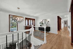 Corridor featuring ornamental molding, a notable chandelier, and light hardwood / wood-style floors