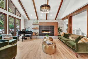 Living room featuring high vaulted ceiling, a tiled fireplace, beam ceiling, and light hardwood / wood-style flooring