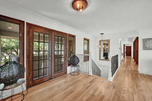 Entrance foyer featuring light wood-type flooring, a chandelier, crown molding, and french doors