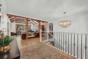 Hallway with light wood-type flooring, an inviting chandelier, and vaulted ceiling with beams