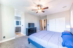 Carpeted bedroom with ensuite bathroom, ceiling fan, and a closet