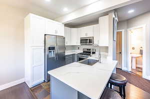 Kitchen with a kitchen breakfast bar, light stone countertops, dark hardwood / wood-style flooring, stainless steel appliances, and sink