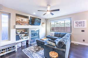 Living room with a textured ceiling, dark wood-type flooring, ceiling fan, and a fireplace