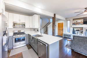 Kitchen with white cabinets, stainless steel appliances, dark hardwood / wood-style floors, kitchen peninsula, and ceiling fan