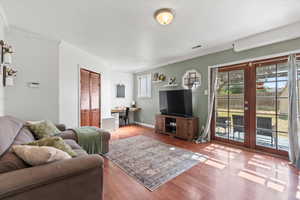 Living room with laminate wood-style flooring, ornamental molding, and french doors