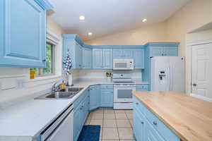 Kitchen with lofted ceiling, white appliances, blue cabinetry, and sink