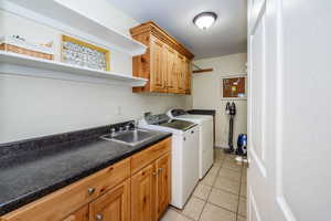 Clothes washing area featuring washer and dryer, cabinets, sink, and light tile patterned flooring