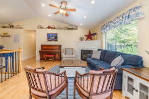 Living room featuring light wood-type flooring, ceiling fan, a fireplace, and vaulted ceiling